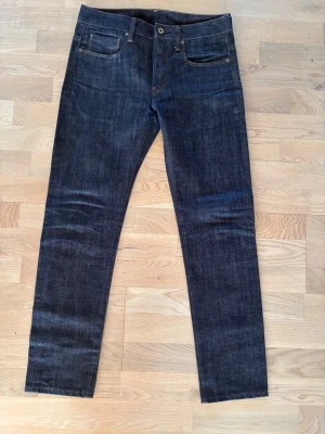 G-Star Raw Mörkblå raka jeans  - Säljer ett par mörkblå jeans från G-Star. Jeansen har kontrastsömmar och knappgylf. Perfekta för dig som gillar en stilren och tidlös look.