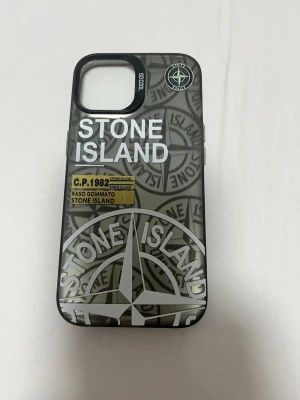 Stone Island mobilskal grå/svart - Snyggt mobilskal från Stone Island i grått och svart med tydlig logga och grafiskt mönster. Skalet har detaljer i vitt samt öppningar för knappar och kamera. Passar till iPhone 13 14 
