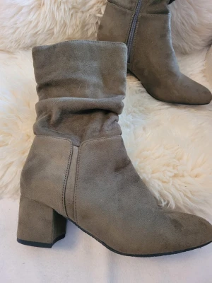 Gröna mockastövletter med klack - Snygga gröna stövletter i mockaimitation med bred klack och slouchy skaft. Dragkedja på insidan för enkel påtagning. Perfekta till jeans eller klänning för en trendig look.