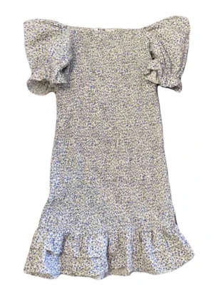 Blommig kortklänning med volang - Slutsåld NAKD klänning. Supersöt kortklänning med småblommigt mönster i blått och lila på vit botten. Klänningen har puffiga korta ärmar och volang nertill för extra flörtig känsla. Perfekt för varma dagar och har en feminin, figurnära passform.