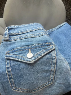 Blå jeans med ficklock och knapp - Snygga blå jeans i klassisk modell med ficklock och silverfärgad knapp. Från Gina 