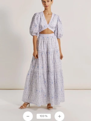 Vit blommig omlottklänning By Malina - Vit omlottklänning från By Malina med lila och blått blommönster. Klänningen har puffiga trekvartsärmar, v-ringning och volangdetaljer längs kanterna. Tillverkad i bomull och perfekt för sommarens alla tillfällen.