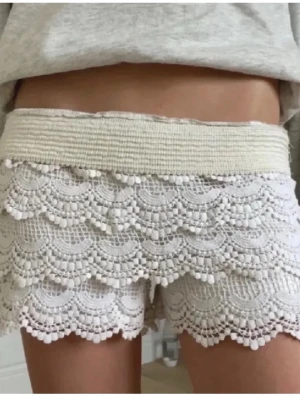 Vita spetsiga shorts med volang - Superfina vita shorts med bred resår i midjan och lager av spets med volangdetaljer. Perfekta för sommaren och ger en söt och romantisk look. Shortsen har en feminin design med dekorativa kanter och är riktigt bekväma.