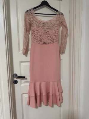 Rosa spetsklänning från Gossip - Supersöt rosa klänning från Gossip med spets upptill och trekvartsärm. Klänningen har en volang nertill och är figurnära med en mjuk, feminin look. Perfekt för dig som gillar romantisk stil och vill sticka ut lite extra.