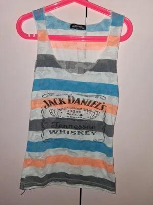 Randig Jack Daniel's linnetopp - Snygg ärmlös linnetopp från Jack Daniel's med breda ränder i blått, orange, grått och vitt. Tryck framtill med Jack Daniel's Tennessee Whiskey-logga. Perfekt för en avslappnad och cool stil.