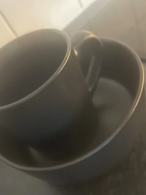 Svart kopp och skål i keramik - Säljer en stilren svart kopp med matchande skål i keramik. Båda har en matt finish och enkel, rund form som passar perfekt till fika eller frukost. Koppen har ett bekvämt handtag och skålen är lagom stor för yoghurt eller snacks.