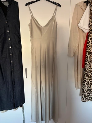 Lång champagnefärgad satinklänning - Elegant långklänning i champagnefärgad/ljus grön satin med smala axelband och v-ringning. Balklänning!