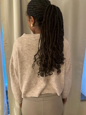 Beige stickad tröja med lös passform - Mysig beige stickad tröja med avslappnad, boxig passform och bred ribbad krage. Tröjan har långa ärmar och är tillverkad i ett mjukt, melerat material som känns skönt mot huden. Perfekt för lager-på-lager och enkel att matcha med olika outfits. Använd ett par gånger och är i storlek S, PRIS KAN DISKUTERAS