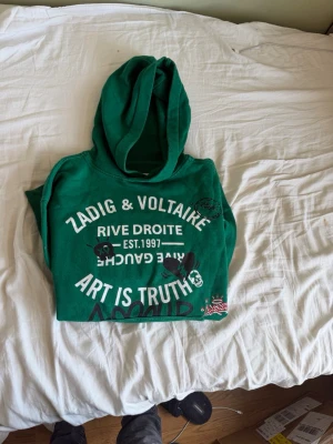 Zadig & Voltaire hoodie - Snygg grön hoodie från Zadig & Voltaire med tryck framtill och coola grafiska detaljer. Stor huva och magficka. Texten 'Art is truth' och 'Rive Droite' ger en unik vibe. Perfekt för dig som gillar streetstyle och vill sticka ut.