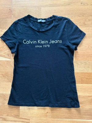 Svart Calvin Klein T-shirt - Använd en del men ändå i bra skick. Bilden längst bak visar 2 ställen där tråden lossnat. Färgen har bleknat. Annars helt ok! Se sista bilden på det som lossnat.