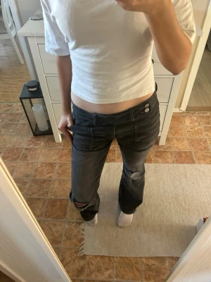 Svarta bootcut jeans med slitningar - Säljer ett par jeans då de är för stora. Jeansen är svarta bootcut med låg midja och slitningar på knäet. Jeansen har dubbla knappar i midjan och klassiska fickor både fram och bak. Säljer för 250kr då de bara är använda två gånger. Ord. Pris: 350kr🩷 