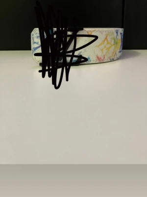 Vitt bälte med färgglada detaljer - Snyggt vitt bälte med färgglada mönster i blått, gult och rött. Bältet har en klassisk form och är perfekt för att ge outfiten en unik touch. Passar dig som gillar accessoarer med lite extra färg.