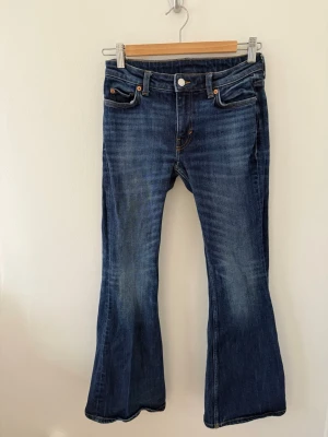 Blå bootcut jeans från weekday  - Säljer ett par klassiska blå bootcut jeans från weekday . Jeansen har fem fickor, normalhög midja och snygga slitningar framtill. Tillverkade i denim med en cool tvätt och kontrastsömmar. Perfekta för en avslappnad och trendig look.