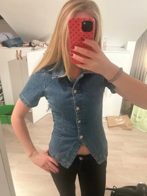 Kortärmad jeanstopp från Gina Tricot - Säljer en snygg kortärmad jeanstopp från Gina Tricot i blå denim. Skjortan har figurnära passform, klassisk krage och knappar framtill. Perfekt till ett par svarta jeans eller kjol för en cool look. Endast använd 1 gång!