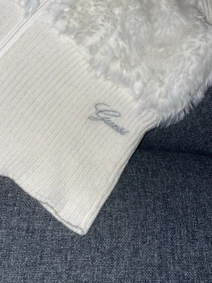 Vit ziptröja med päls från Guess - Säljer en vit ziptröja från Guess med ribbstickade ärmar och nederdel samt mjuk päls på bröstet. (Säljer pga flytt, pris kan diskuteras) 