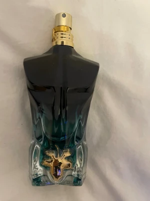 Le beau Le Parfum från Jean Paul Gaultier - Unik parfymflaska formad som en manlig torso i svart och blått glas med gulddetaljer och en dekorativ guldfärgad hjort på framsidan. Flaskan har en lyxig känsla och står på en rund röd sammetsbas. Perfekt för dig som gillar statement-dofter. 75 ml Jean Paul Gaultier Le Beau Le Parfum.