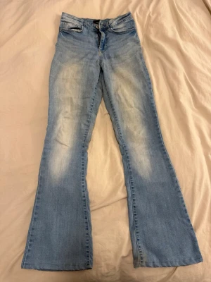 Ljusblå bootcut jeans med slitningar - Säljer ett par ljusblå bootcut jeans med snygga slitningar framtill. Jeansen har klassisk femficksdesign, normal midja och utsvängda ben. Perfekta för dig som gillar retrovibbar och vill ha ett par bekväma jeans i mjukt denimtyg.