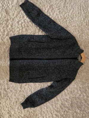 Mörkblå stickad ziptröja - Mysig mörkblå stickad ziptröja med ribbade muddar. Insidan har ett rutigt foder i brunt, vitt och svart som ger extra värme och stil. Perfekt för kyliga dagar och enkel att matcha med olika outfits. Den är inte använd en ända gång.