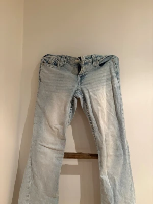 Ljusblå bootcut jeans True Religion - Säljer ett par ljusblå bootcut jeans från True Religion med slitna detaljer och klassiska kontrastsömmar. Jeansen har två fickor fram och två bakfickor med lock och dekorativa sömmar. Perfekta för en avslappnad och trendig look.
