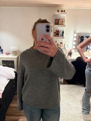 Grå stickad tröja med rund hals - Mysig grå stickad tröja med rund halsringning och långa ärmar. Tröjan har en enkel och avslappnad passform, perfekt att matcha med jeans eller kjol. Materialet ser ut att vara mjukt och bekvämt, perfekt för kyligare dagar.