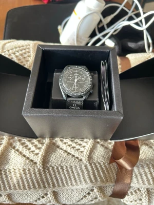 Omega x Swatch mission to moonphase - Snygg svart Omega x Swatch Speedmaster klocka med klassisk rund urtavla och detaljerad kronograf. Mycket bra skick! Box osv följer såklart med. Köpte den på Genèves flygplats och kvittot medföljer!