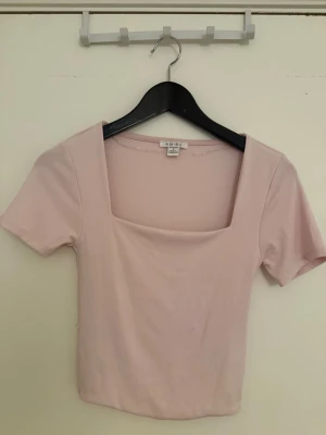 Ljusrosa topp med fyrkantig urringning - Säljer en ljusrosa topp från Amisu med korta ärmar och snygg fyrkantig urringning. Toppen är croppad och har en slim passform som sitter snyggt på kroppen. Perfekt att matcha med höga jeans eller kjol.