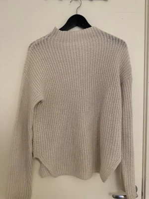 Vit stickad tröja med hög krage - Mysig vit stickad tröja med hög krage och lång ärm. Tröjan har en grovstickad struktur och rak passform, perfekt för lager-på-lager. Enkel och stilren design som passar till det mesta. 