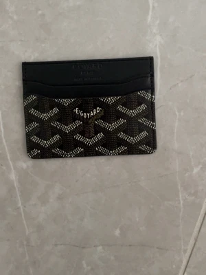  svart kortfodral i läder - Snyggt svart kortfodral med klassiskt mönster i vitt och grått. Tillverkat i läder med flera kortfack och gul insida. Perfekt för dig som vill ha en stilren och exklusiv accessoar i fickan.