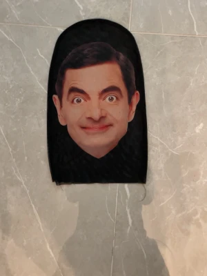 Svart balaklava med Mr Bean - Rolig svart balaklava med tryck av ett ansikte framtill. Perfekt för maskerad eller cosplay. Tillverkad i stretchigt tyg som formar sig efter huvudet. Passar dig som vill sticka ut på festen eller eventet.