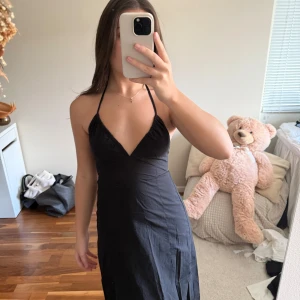 Svart halterneck klänning - Säljer en svart klänning med halterneck och v-ringning. Klänningen har en figurnära passform och är ärmlös med tunna band som knyts i nacken. Perfekt för sommaren och enkel att styla med accessoarer.