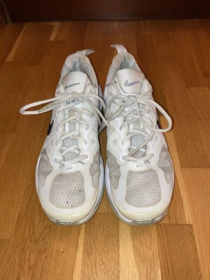 Vita Nike sneakers med meshdetaljer - Säljer ett par vita Nike sneakers med svart swoosh på sidan. Skorna har meshpaneler för extra ventilation och vita snören. Yttersulan är vit med beige inslag och skon har en sportig, låg profil. Perfekta för dig som gillar stilrena och bekväma sneakers. INNESKOR! Snabb affär!
