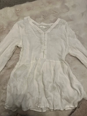 Vit blus med knappar och v-ringning - Supersöt vit blus från 157 med v-ringning och knappar framtill. Blusen har långärmade ärmar med lätt volang vid ärmslut och är gjord i ett tunt, krinklat tyg som ger en avslappnad känsla. Perfekt att styla med jeans eller kjol för en fräsch look.