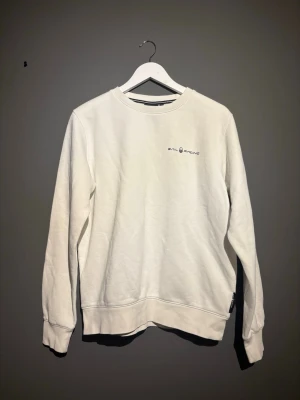 Vit sweatshirt från Sail Racing - Vit sweatshirt från Sail Racing med rund halsringning och diskret logga på bröstet. Tröjan har långa ärmar och är gjord i mjukt bomullsmaterial. Perfekt för en clean och stilren look. 