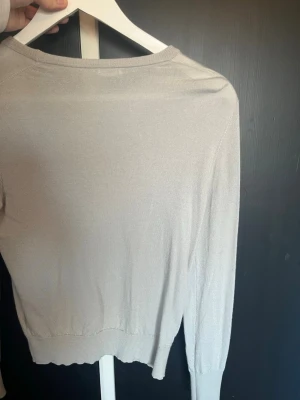 Ljusbeige tunn stickad tröja - Säljer en ljusbeige tunn stickad tröja från Filippa K. Tröjan har rund halsringning, långa ärmar och ribbade muddar vid ärmslut och nederkant. Perfekt basplagg i garderoben och enkel att styla till olika looks.