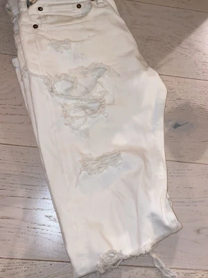 Vita ripped jeans storlek W31 L32 - Säljer ett par vita jeans med flera slitningar och hål på benen för en trendig, avslappnad look. Jeansen har fransiga benslut och klassisk femficksmodell med nitar. Perfekta för dig som gillar streetstyle och vill sticka ut.