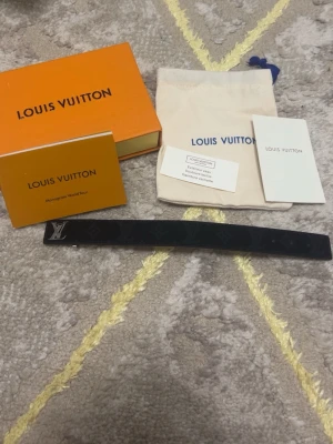 Svart Louis Vuitton armband monogram - Snyggt svart armband från Louis Vuitton med klassiskt monogrammönster och silverfärgad LV-detalj. Armbandet är smalt och stilrent, perfekt för dig som gillar exklusiva accessoarer med ikonisk design. Kommer med original ask och dustbag.