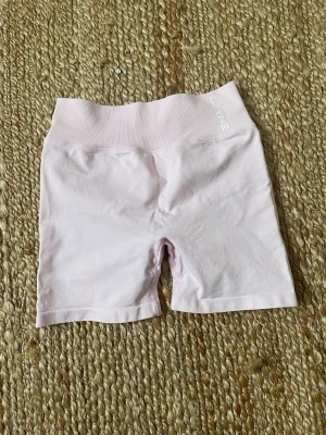 Ljusrosa seamless shorts från DFYNE - Säljer ett par ljusrosa seamless shorts från DFYNE med hög midja och ribbad linning. Shortsen har snygg scrunch-detalj bak och är perfekta för träning eller chill. Materialet är mjukt och stretchigt för bästa komfort.