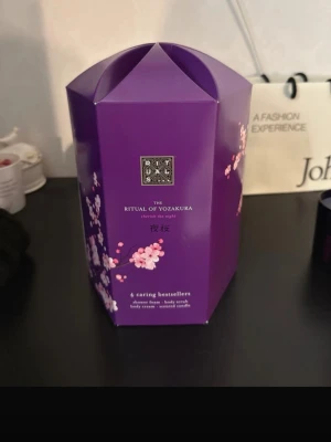Rituals The Ritual of Yozakura kit - Lyxigt presentkit från Rituals i serien The Ritual of Yozakura. Innehåller duschskum, kroppsskrubb, body cream och doftljus. Alla produkter har en elegant lila design med blommotiv och doft av körsbärsblom. Perfekt för dig som vill unna dig något extra till din hudvårdsrutin.