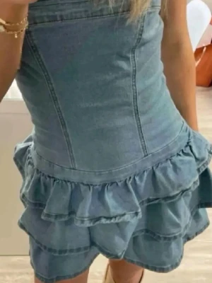 Jeansklänning med volanger - Snygg och trendig axelbandslös jeansklänning i ljusblå denim med figurnära passform och dubbla volanglager nedtill. 