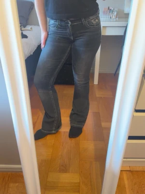 Svarta bootcut jeans med vita sömmar - Säljer ett par svarta bootcut jeans med vita kontrastsömmar och fickor bak med knappdetalj. Jeansen har låg midja och är tillverkade i stretchigt denimtyg. Använd få gånger💕