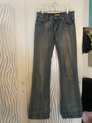 Blå bootcut jeans från Bulldozer - Säljer ett par blå bootcut jeans från Bulldozer. Jeansen har en avslappnad passform och är tillverkade i denim med snygg tvättad look. Har en del fläckar som visas på bilderna, annars inget fel på dem