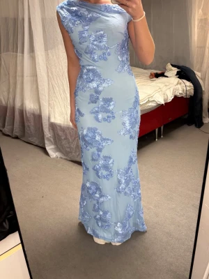 Ljusblå långklänning med blommor - Elegant ljusblå långklänning med stora blommiga applikationer i blått. Perfekt för bal, aldrig använd. Perfekt längd på mig som är 167cm. Köpt på vinted för 1000kr, vet tyvärr inte vart den är ifrån🥹