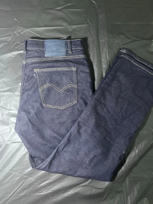 Mörkblå raka jeans från Levi's - Säljer ett par klassiska mörkblå jeans från Levi's med raka ben och kontrastsömmar. Jeansen har fem fickor och en patch med Levi's-logga bak i midjan. Perfekta till en avslappnad streetwear-look.