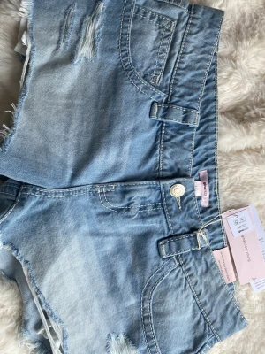 Gina tricot - Säljer ett par ljusblå låg midjade jeansshorts från Gina Tricot. Shortsen har råa kanter, slitningar och bälteshällor. Perfekta för varma dagar och ger en avslappnad look. 