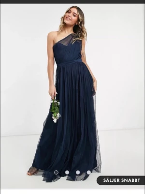 Marinblå långklänning oneshoulder - Säljer denna fina one shoulder klänning som är helt oanvänd med lappen kvar. Har en till annons med en mindre storlek, samma klänning. Köptes 2023 så finns ej att köpa nu. Från asos. Denna klänning är storlek M/L (uk 12). 