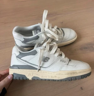 New Balance 550 vita sneakers - Snygga New Balance 550 sneakers i vitt läder med grå detaljer och beige sula. Klassisk retrostil med lågt skaft och tydliga NB-loggor på sidan och tungan. Perfekta för dig som gillar stilrena och tidlösa sneakers.