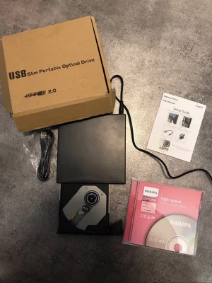 USB Slim portable Optical drive + 5 st dvd-rw - Slimmad extern optisk enhet med USB 2.0-anslutning, perfekt för att läsa och bränna CD och DVD. Kommer i svart plast med tillhörande kabel, installationsguide och en 5 st Philips DVD-RW skiva. Enkel att koppla till datorn via USB.
