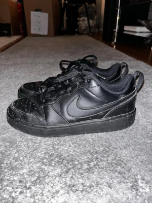 Svarta Nike sneakers i läder - Säljer mina snygga helsvarta Nike sneakers i lågt modell med klassisk swoosh på sidan. 💕