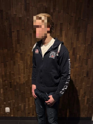 Marinblå hoodie från Vinson Polo Club - Mörkblå hoodie med dragkedja från Vinson Polo Club. Stor vit text på ena ärmen, amerikansk flagga och klubbmärke på bröstet. Huva med vita snören och två fickor framtill. Riktigt stillren och fräsch hoodie! Skick 9/10 inga defekter, nyskick! Modellen är 180cm och väger 73kg, och tröjan sitter lite litet på han skulle säga att den passar 170-178cm! Hör av er vid intresse, pris går att diskutera!🤩