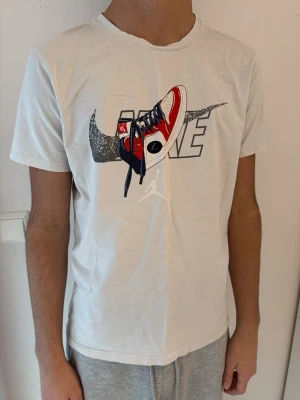 Nike t-shirt - Säljer en vit t-shirt från Nike med ett stort tryck av en röd och vit sneaker och Nike-logga på bröstet. T-shirten har korta ärmar och normal passform. Baksidan har en liten Nike-detalj upptill. Storleken stämmer ej, skulle säga den passar XS-S
